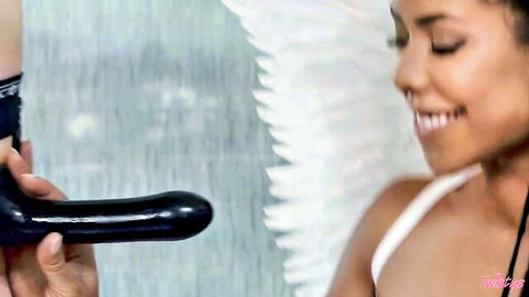 Kira Noir as sexy angel smiling while holding black strap-on dildo