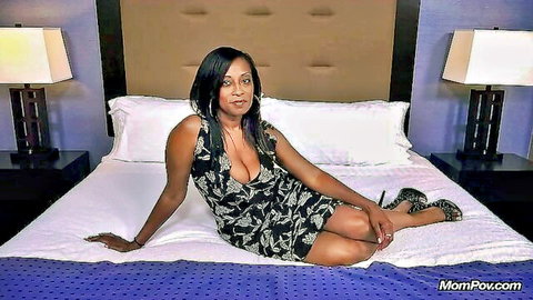 Curvy ebony MILF with massive tits in deep cleavage dress lounging seductively on bed