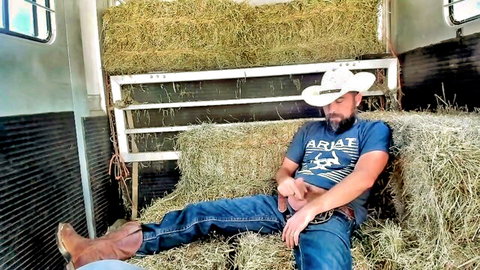 Rugged bearded cowboy napping on hay in jeans, hand near bulge