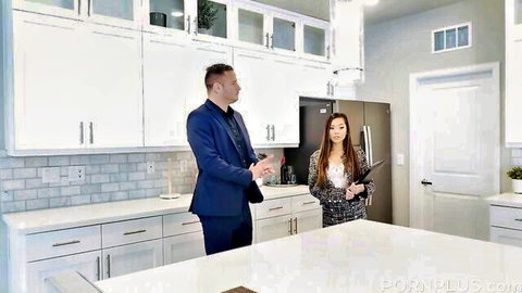Suited man talks to petite Asian realtor in tight skirt holding tablet in modern kitchen