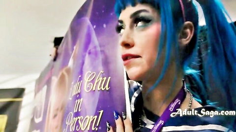 Blue-haired cosplay babe Chi Chuh pouting seductively holding poster at adult con