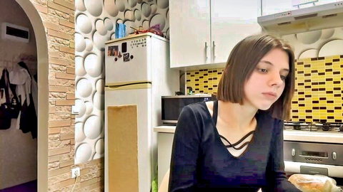Cute young teen girl in black low-cut top teasing cleavage in kitchen webcam