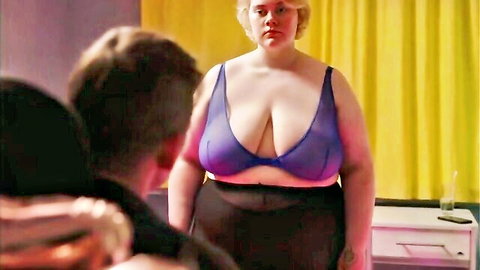 Blonde BBW with huge tits in sheer purple bra stands over man staring at her cleavage