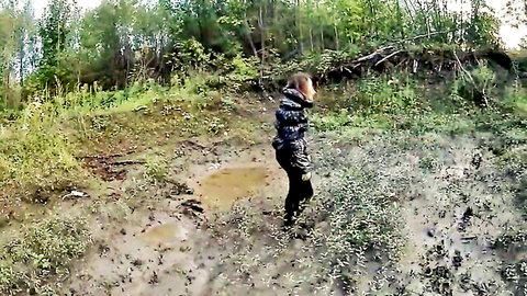 Blonde woman in camo jacket wading through muddy forest trail