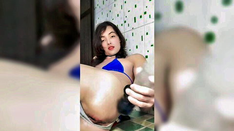 Asian woman in blue bikini pulls aside bottoms to fuck shaved pussy with purple dildo in bathroom