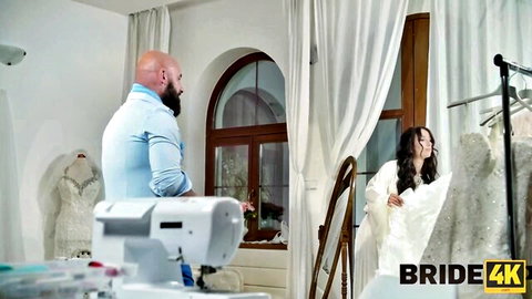 Sexy long-haired Asian bride in white wedding gown with muscular bearded tailor in bridal shop