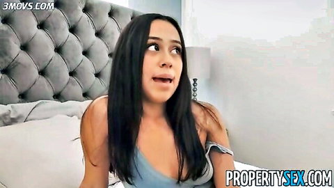 Brunette Latina real estate agent in low-cut blue top showing cleavage on bed