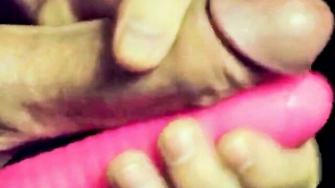 Hand gripping erect cock pressed against thick pink dildo closeup