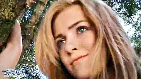 Blonde beauty with green eyes smirks seductively up close in lush outdoor forest