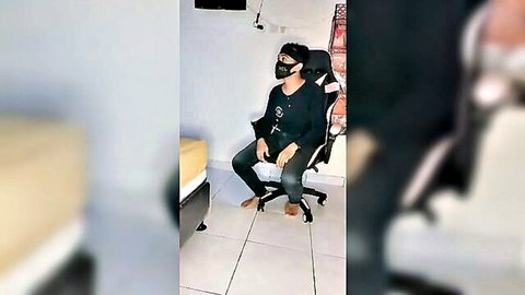 Amateur Indonesian masked guy in black hoodie sits legs spread barefoot in gaming chair