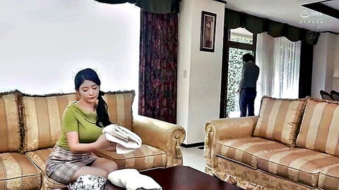 Japanese wife in short plaid skirt spreads legs on couch holding white panties with husband in background