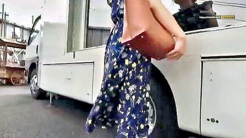 Asian woman in floral sundress holding bag by white van outdoors