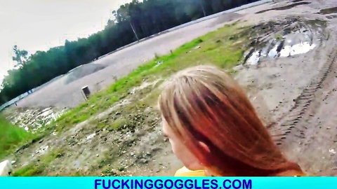 Blonde babe in yellow top smiling back at camera in muddy outdoor dirt track