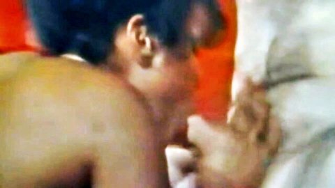 Blurry close-up of Asian woman with black hair leaning intimately over white sheets in orange-lit scene