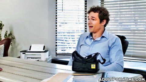 Curly haired man in blue shirt smiling in office holding black bag