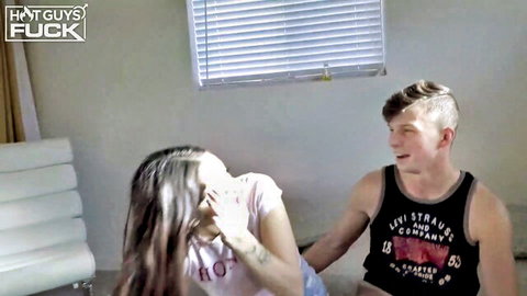 Shocked brunette teen covers mouth while sitting close to young guy on couch in teasing scene