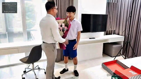 Asian teacher in suit hands flowers to smiling schoolboy in uniform for graduation