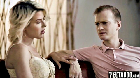 Blonde MILF in low-cut dress touched on arm by young guy on couch in taboo stare-down