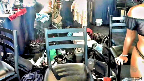 Ebony camgirl in sheer black top and thong grabs chair in messy cluttered room
