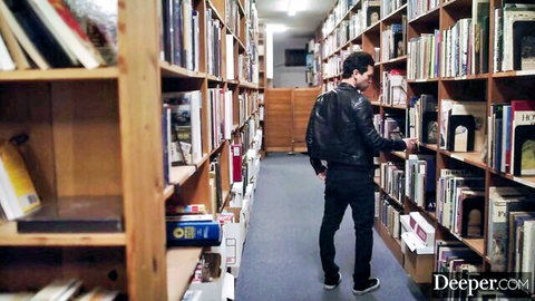 Curly-haired man in leather jacket browsing bookshelves in library