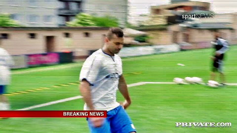 Muscular soccer player in white jersey and blue shorts dribbling ball on green field during breaking news broadcast