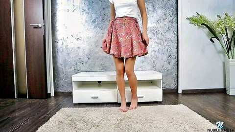 Taylor Krystal in white top and floral mini skirt, standing barefoot seductively