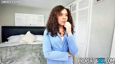 Curly haired ebony real estate agent in tight blue blazer poses thoughtfully in bedroom