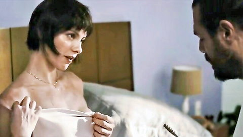 Brunette woman nude from shoulders up holding white sheet over medium tits talking to bearded man in bed