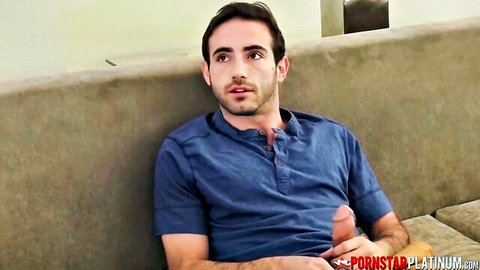 Handsome man in blue shirt strokes his hard cock sitting on beige couch