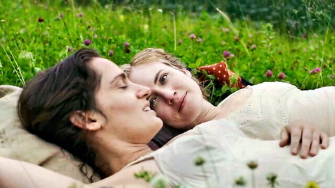 Blonde woman cuddles intimately with brunette lover in lush green field outdoors