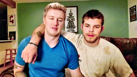 Two muscular white guys embracing intimately, one blonde in blue shirt