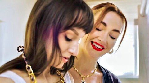 Two pretty women, brunette and blonde, smiling intimately with gold jewelry, previewing Seth Gamble sex scene