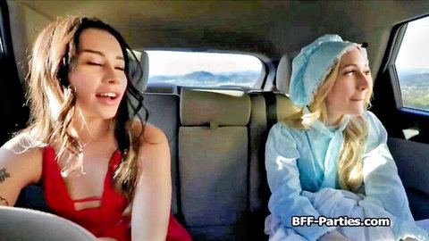 Brunette in red dress and blonde in blue outfit smile seductively in car backseat, introducing Emma to foursome