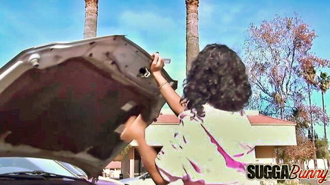 Sexy ebony babe with curly hair bends over open car trunk teasing her ass outdoors