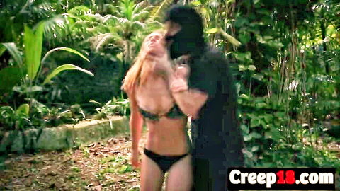 Raylin Ann in bikini held by masked stranger in jungle bondage scene