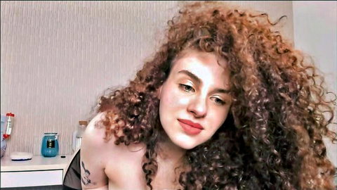 Curly haired young teen with big tits smiling seductively topless on webcam solo