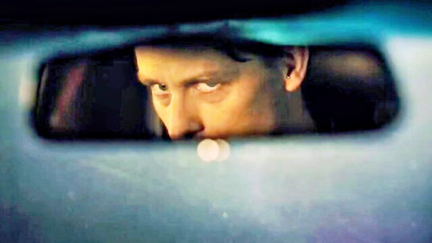 Intense man with furrowed brows staring through car rearview mirror in dramatic blue-lit closeup