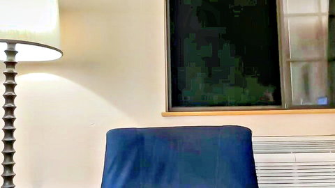 Empty bedroom corner with blue chair, spiral lamp, dark window and AC unit.