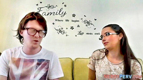Nerdy British redhead guy in glasses faces busty brunette woman on couch with family wall decal