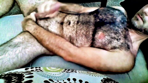 Hairy bearded DILF gets amateur handjob from young man on couch exposing crotch