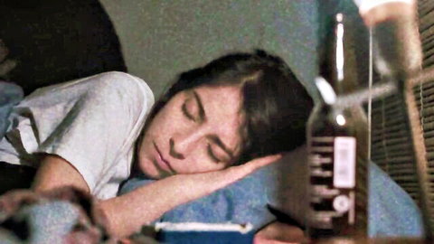 Brunette woman sleeping in loose white t-shirt on bed next to beer bottle