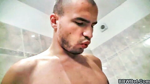 Shirtless muscular bald man with goatee puckers lips teasing in tiled bathroom