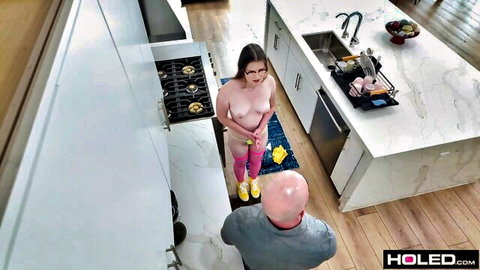 Brunette with glasses stands nude in kitchen as bald man kneels below eyeing her pussy