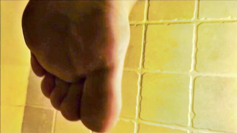 Close-up of bare foot sole with toes spread against yellow tiled shower wall for foot worship