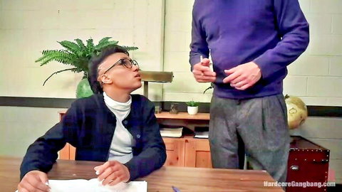 Ebony guy in glasses sits at office desk looking up at tall man in purple sweater holding cigarette