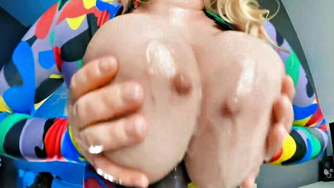 Blonde with massive shiny oiled tits squeezed together exposing erect nipples in colorful bodysuit