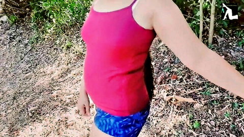 Slim Asian beauty in pink tank top and blue shorts outdoors in wilderness