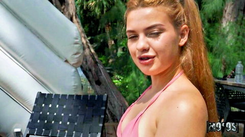 Sexy redhead teen in skimpy pink bikini posing outdoors by pool floats