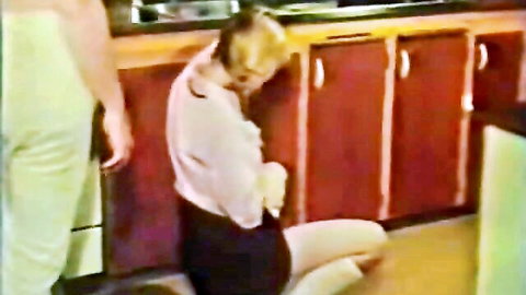 Vintage blonde woman in blouse and skirt kneeling before man in classic 70s porn scene