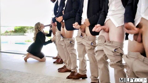 Cory Chase kneeling before line of suited men with exposed big black cocks